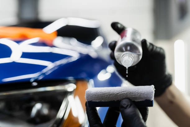 Installer applying ceramic coating with an applicator pad over paint protection film on a blue car