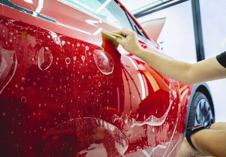 Installer squeegeeing paint protection film onto the door of a red car